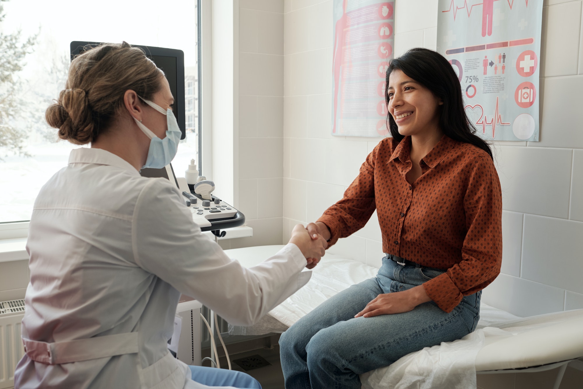 Female clinician shaking hand of young happy Hispanic patient